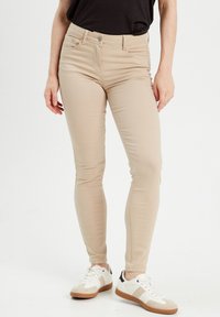 Jean skinny beige en tissu extensible en mélange de coton, avec un design classique à cinq poches et une fermeture à bouton à l'avant.