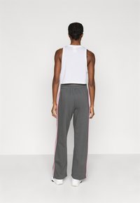 Szare spodnie dresowe z różowymi paskami po bokach, elastyczną talią oraz krótki biały top na ramiączkach, widziane od tyłu. Gładka tekstura, casualowy design.