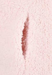 Material rosa y esponjoso con una superficie texturada y una costura que muestra una hendidura abierta. La tela parece suave y acolchada, con un aspecto acogedor.