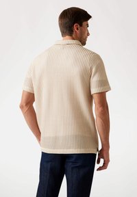 Short-sleeve knit polo shirt in beige with textured vertical stripes. Features a collared neck and side slits at the hem.