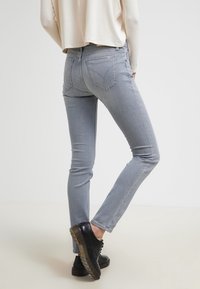 Světlé šedé džíny ve slim fit, s mírným elastickým efektem, s zadními kapsami a jemnými švy. V kombinaci s černými šněrovacími botami.