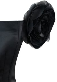 Abito nero con un corpino aderente e un grande fiore a strati in tessuto nero come accentuazione sulla spalla. Tessuto liscio, design senza maniche.