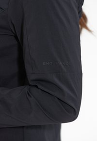 Top atletico a maniche lunghe nero con una texture liscia, caratterizzato da un discreto logo ENDURANCE sulla manica sinistra.