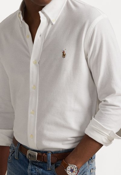 White button-up shirt with long sleeves, made from textured fabric. Features a small multi-colored embroidered logo on the chest.