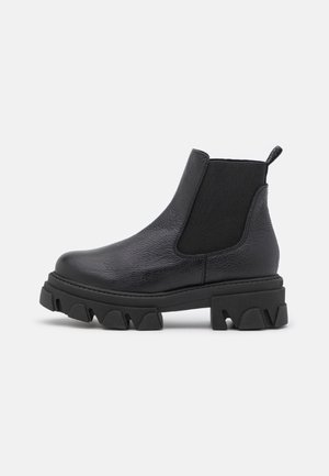 Black leather Chelsea boot with chunky lug sole, elastic side panels, and pull tab at the back, shown in side profile on white background.