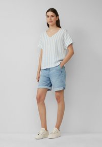Jasnoniebieska bluzka w białe paski z mieszanki lnu z dekoltem w serek, w zestawie z jasnymi dżinsowymi szortami z podwiniętymi mankietami i białymi trampkami.