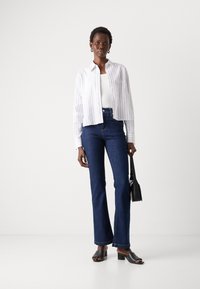 Hvit- og blåstripet skjorte, hvit topp, mørkeblå vide jeans, svarte blokkhæl sandaler og en liten svart skulderveske.