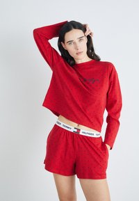 Röd långärmad topp och matchande shorts med svarta prickar. Toppen har en avslappnad passform; shortsen har en elastisk midja med varumärkeslogga.