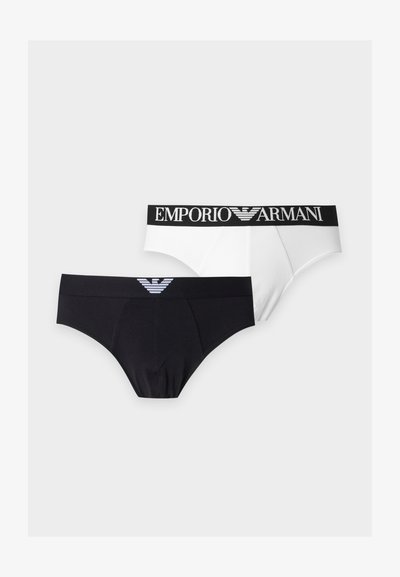 Δύο ανδρικά εσώρουχα Emporio Armani, ένα μαύρο με λογότυπο μπροστά, ένα λευκό με λογότυπο στη ζώνη, απεικονίζονται σε απλό ανοιχτό φόντο.