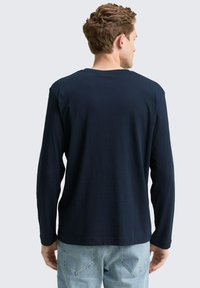 Marineblauwe lange mouwen shirt van lichtgewicht stof, met een ronde halslijn en een ontspannen pasvorm, met zichtbare naden en een gladde textuur.