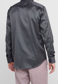 Camicia a maniche lunghe grigio scuro realizzata in tessuto liscio, con colletto a punta, polsini con bottone e orlo curvo.