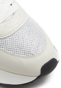 Zapatilla blanca de cuero con parte superior de malla plateada texturizada y suela de goma negra. Incluye cordones blancos y una tapa de puntera lisa.