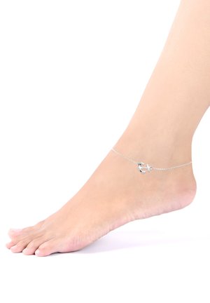 Cavigliera in argento con un piccolo charm a forma di ancora, design della catena delicato, su un piede nudo, isolato su uno sfondo bianco.