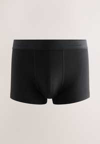 Boxers noirs avec une large ceinture ornée d’un texte subtil et répétitif "Next Signature" sur un fond clair uni.