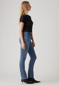 T-shirt noir court associé à un jean bleu taille mi-haute. Le jean présente un design classique à cinq poches et est légèrement décoloré. Des bottines noires viennent compléter le look.