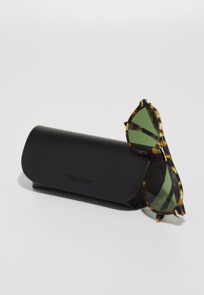 Ochelari de soare tortoise brown cu lentile verzi, cu accente ascuțite, poziționați lângă un etui rectangular negru, embosat cu "Giorgio Armani".