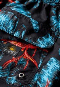 Tessuto nero con un vivace motivo floreale blu e rosso. Presenta un'etichetta con il logo "Superdry" e un dettaglio con bottone automatico.