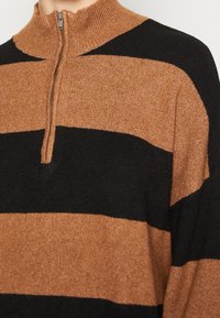 Maglione a righe marroni e nere con colletto alto e chiusura a mezza zip, caratterizzato da una texture morbida e da motivi orizzontali a contrasto.