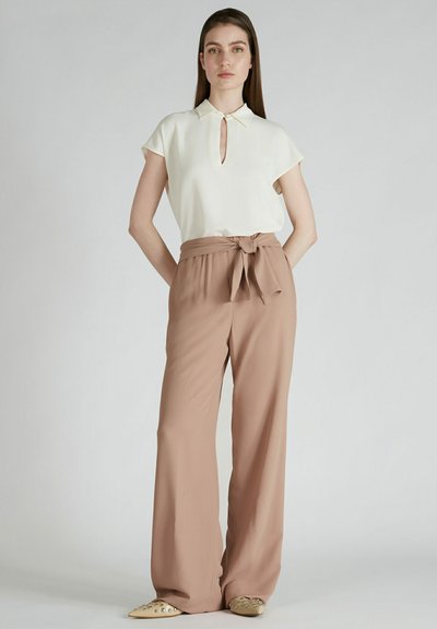 Witte blouse met korte mouwen en een keyhole-halsdetail, gecombineerd met lichtbruine hoge taillebroeken en beige puntige ballerina's. Glad stoftextuur.