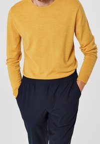 Mosterdgele, trui met ronde hals in een gestructureerde brei, gecombineerd met donkerblauwe, broek met elastische taille en zijzakken.