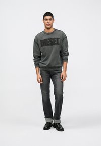 Sweatshirt cinza escuro com grande logo preto "DIESEL", combinado com jeans escuros e sapatos pretos. Fit relaxado e jeans com as bainhas dobradas.