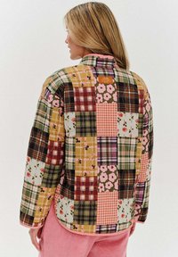 Překližovaná bunda s patchworkovým vzorem, který kombinuje různé květinové a kostkované motivy v barvách jako zelená, růžová, hnědá a žlutá.