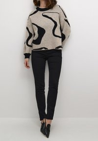 Crème kleurige pullover trui met zwarte abstracte patronen, voorzien van een ronde hals en ribgebreide manchetten. Gepaard met zwarte slim-fit broek en puntige schoenen.