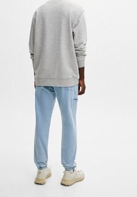 Sweat-shirt gris avec poignets et ourlet côtelés, associé à un pantalon de jogging bleu clair avec taille élastique, et des baskets beiges.