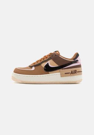 Brown and beige Nike Air Force 1 sneaker with black swoosh, peach accents, thick beige sole, and "AIR" label on the heel.