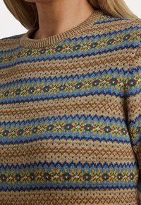 Stickad tröja med rund halsringning, texturerad brun bas och mönstrade ränder i blått, grönt och rosa.