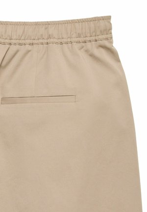 Pantalon beige à taille élastique avec une poche passepoilée unique à l'arrière, en tissu lisse.