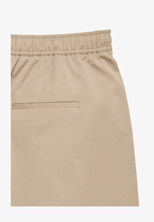Pantalon beige à taille élastique avec une poche passepoilée unique à l'arrière, en tissu lisse.