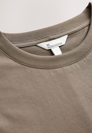 T-shirt marron en coton à col rond avec une texture lisse. Comprend une étiquette d'entretien imprimée sur une étiquette blanche à l'intérieur du col.