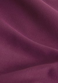 Lila Stoff mit einer glatten, matten Textur, der sanfte, fließende Falten aufweist und eine gleichmäßige Farbe ohne Muster oder Details hat.