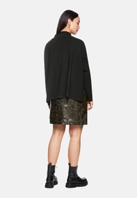 Schwarzer oversized Pullover mit hohem Kragen, kombiniert mit einem glänzenden grünen Leopardenmuster-Rock. Das Model trägt schwarze Stiefeletten mit Nieten.
