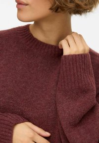 Bordo pleteni džemper s rebrastim okruglim izrezom i rukavima, izrađen od mekanog materijala s teksturiranim završetkom. Krupni plan gornjeg dijela tijela.