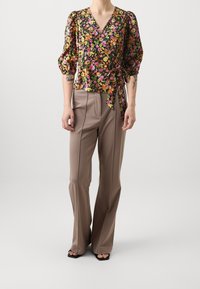 Blusa floreale nera con maniche a sbuffo e scollatura a V, abbinata a pantaloni beige a vita alta con pieghe verticali e vestibilità ampia.