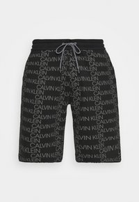 Czarne szorty z nadrukiem logo CALVIN KLEIN na całej powierzchni, wykonane z gładkiego materiału, z elastycznym paskiem w talii i sznurkiem do regulacji, o standardowym kroju.