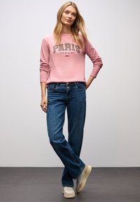 Różowy sweter z nadrukiem "PARIS", w połączeniu z niebieskimi spodniami typu straight-leg. Wykończony beżowymi sneakersami, prosty fason i miękki materiał.