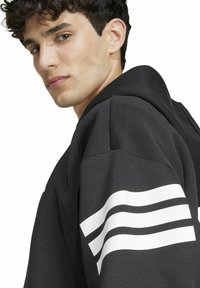 Felpa nera con ampie strisce bianche sulla manica sinistra, realizzata in un tessuto morbido, con una vestibilità comoda e design con cappuccio.