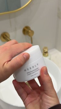 Pot blanc étiqueté "NEEDLY Baume nettoyant doux" avec du texte noir. Contient 120 ml, présente une surface lisse, une forme ronde et une légère courbure sur le couvercle.
