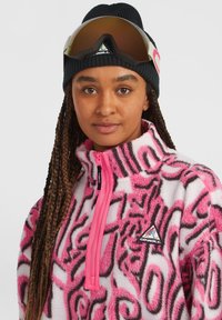 Fleece pullover in pink with black and white abstract patterns, featuring a high collar, half-zip, and a black beanie with goggles on top.