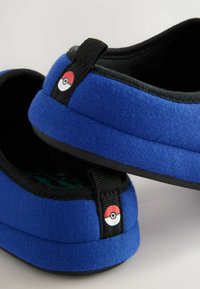 Blå lærredssandaler med sort kant og sål, med et Poké ball-emblem på hælen og blød tekstiloverflade.