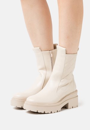 Bottines en cuir beige avec un design matelassé sur les côtés, une fermeture éclair sur le côté et une semelle plateforme épaisse avec un type de crampons.