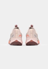 Rückansicht von beigen Sportschuhen mit pinken Akzenten. Texturiertes Material, reflektierende Details und eine robuste Gummisohle.