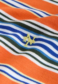 Oranža adīta auduma ar horizontālām zilām, baltām un zaļām joslām, centrā neliels dzeltenā izšūts burts "N" un "V", kas pārklājas.