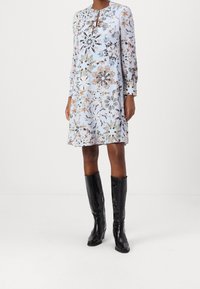 Vestido de estampado floral con mangas largas, escote redondeado y detalle en forma de ojal, en azul claro, que presenta patrones y acentos intrincados.