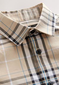 Beiges kariertes Hemd mit abwechselnden schwarzen, weißen und hellblauen Linien, einem spitzen Kragen und zwei schwarzen Knöpfen vorne.