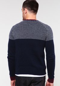 Navy knit sweater with white zigzag pattern on the upper section. Ribbed burgundy cuffs and hem, standard fit, smooth texture.