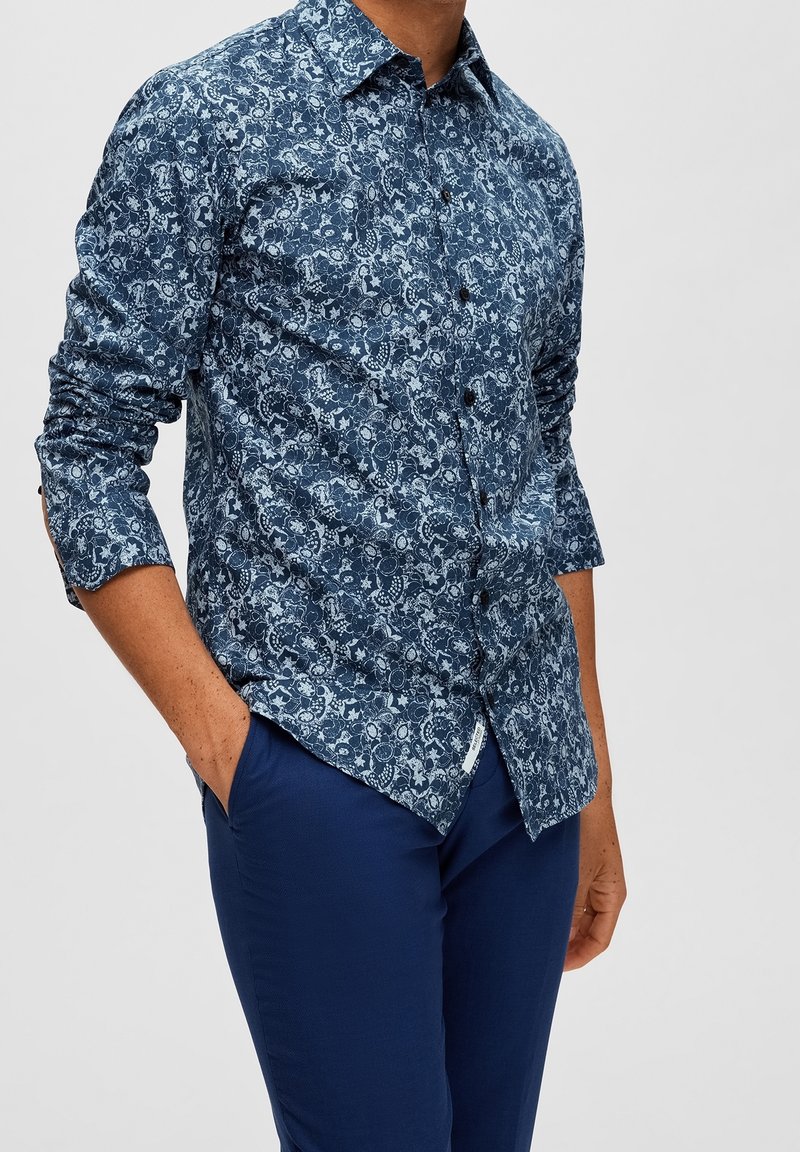 Mörkblå knäppskjorta med paisleymönster, tillverkad av lättviktsmaterial. Långa ärmar med knappmanchetter, något rundad fåll.